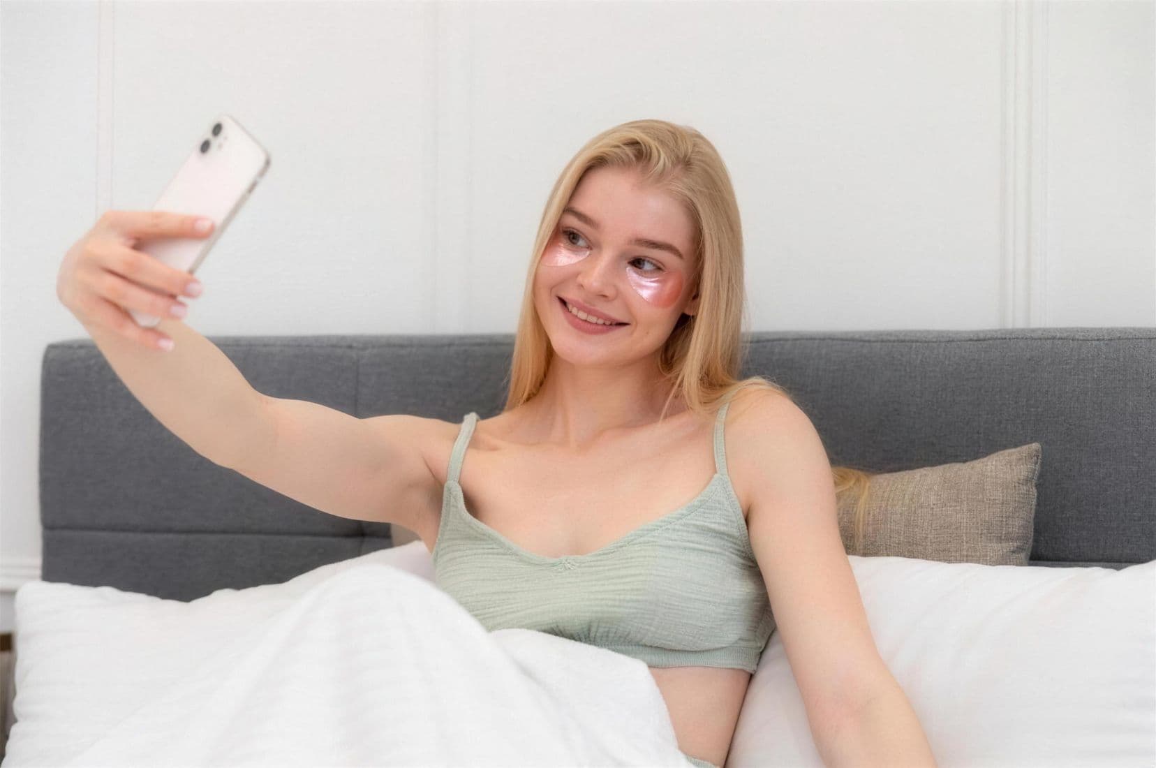 Frau macht Selfie im Bett mit Augenmasken.
