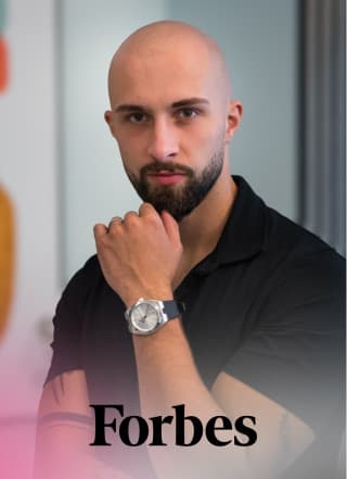 Mann mit Bart und Uhr posiert vor Forbes-Logo.
